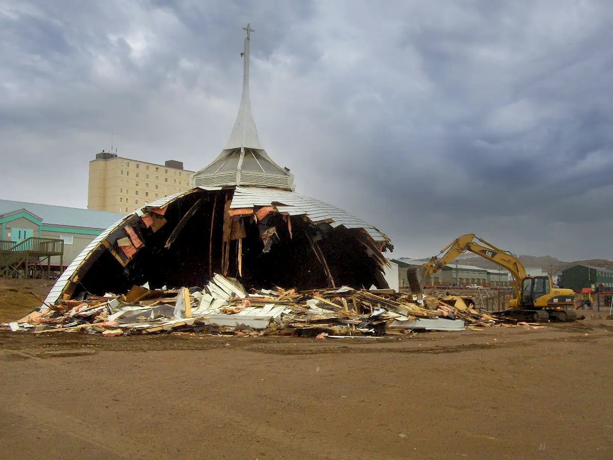 Demolición del domo original de la iglesia mediante maquinaria pesada, despejando el sitio para la futura estructura espacial Triodetic en una comunidad ártica.