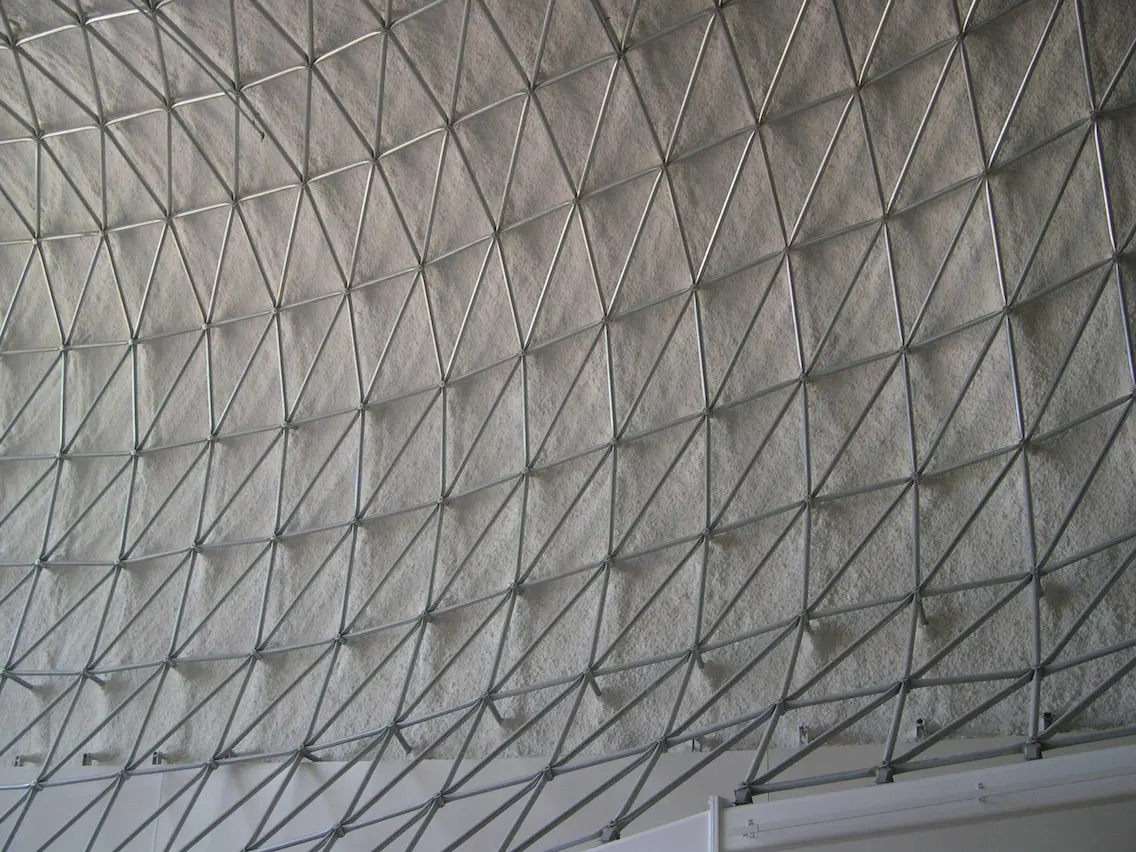 Vista interior de un domo industrial con paneles de aislamiento blanco soportados por una estructura espacial de acero. La geometría triangular muestra precisión en ingeniería, diseño liviano y resistencia para aplicaciones mineras y de almacenamiento.