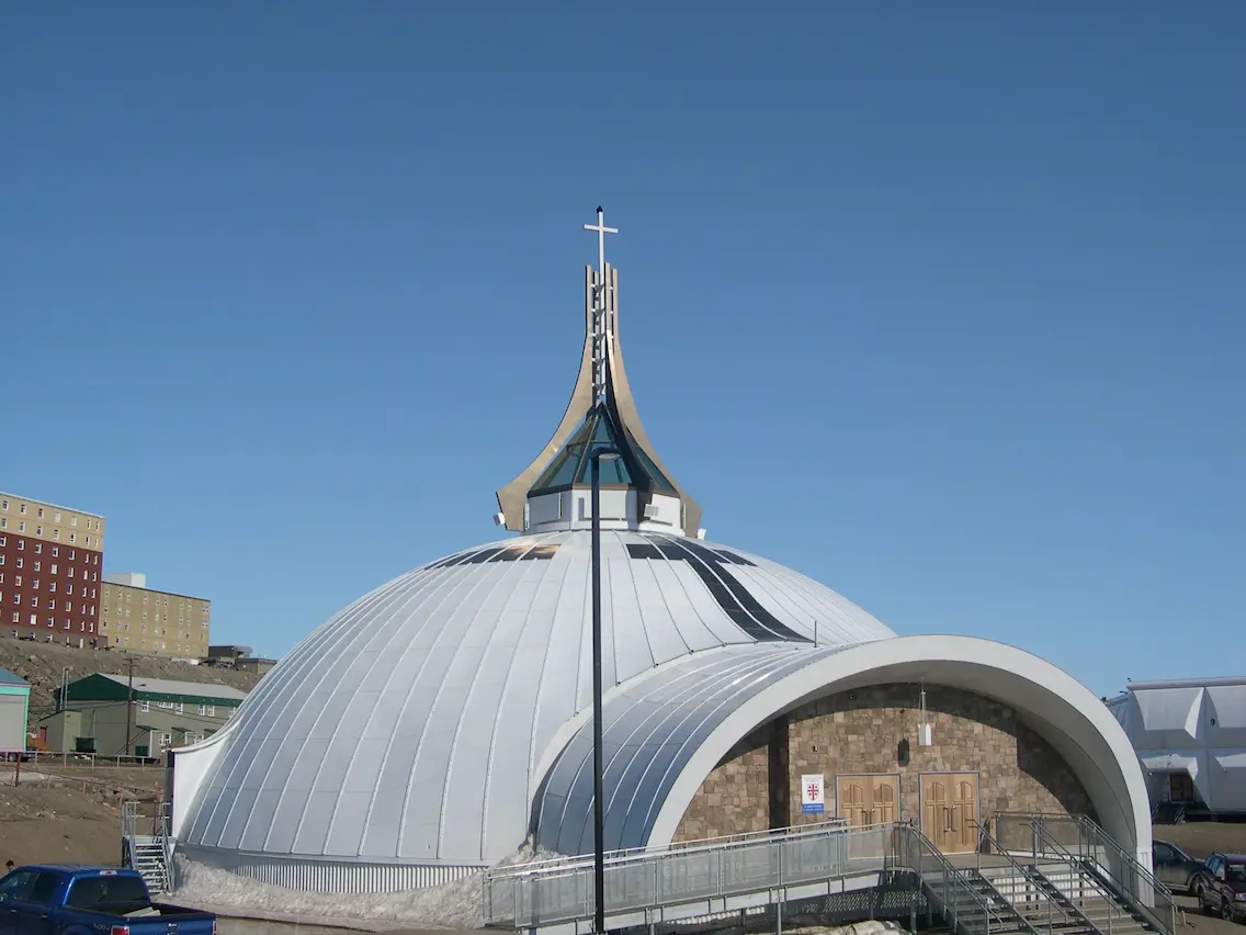 Vista exterior de la Catedral de San Judas en Iqaluit, mostrando la estructura Triodetic de acero y aluminio con una aguja coronada por una cruz y entrada curva.