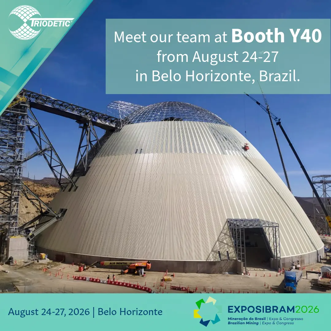 un domo industrial blanco de gran tamaño, estructura espacial de acero, instalación de almacenamiento minero, vista aérea, estructura transportadora al lado izquierdo, patio de grava con camiones y equipos, banner PDAC 2026 superpuesto, convención minera en Toronto Canadá, paneles metálicos de revestimiento, techo circular con aperturas de ventilación