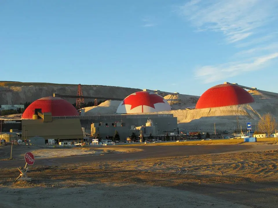 Trois dômes miniers rouges Triodetic utilisés pour le stockage de matériaux en vrac et le contrôle de la poussière, situés dans une installation minière industrielle au coucher du soleil.