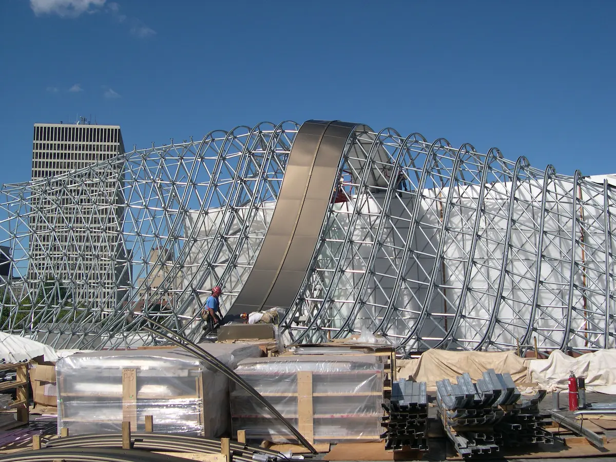 Estructura space frame de acero tipo bóveda de cañón en proceso de construcción en un entorno urbano, mostrando geometría curva, ensamblaje modular y sistema de instalación para cubiertas de gran luz.