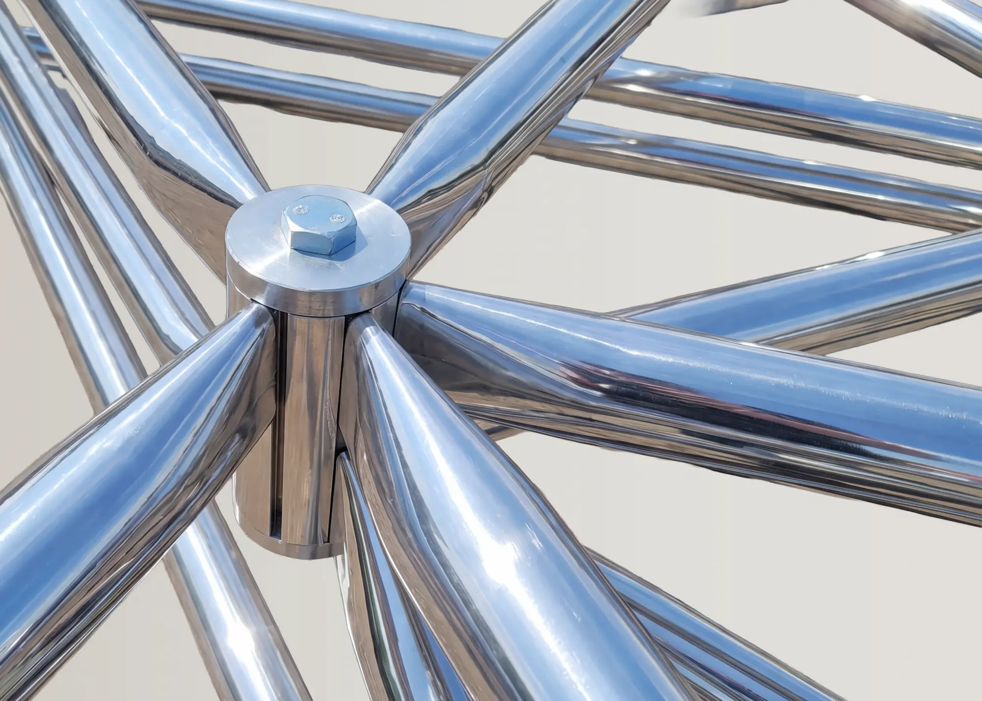 Triodetic core connecting polished metal tubes around a central bolted hub.